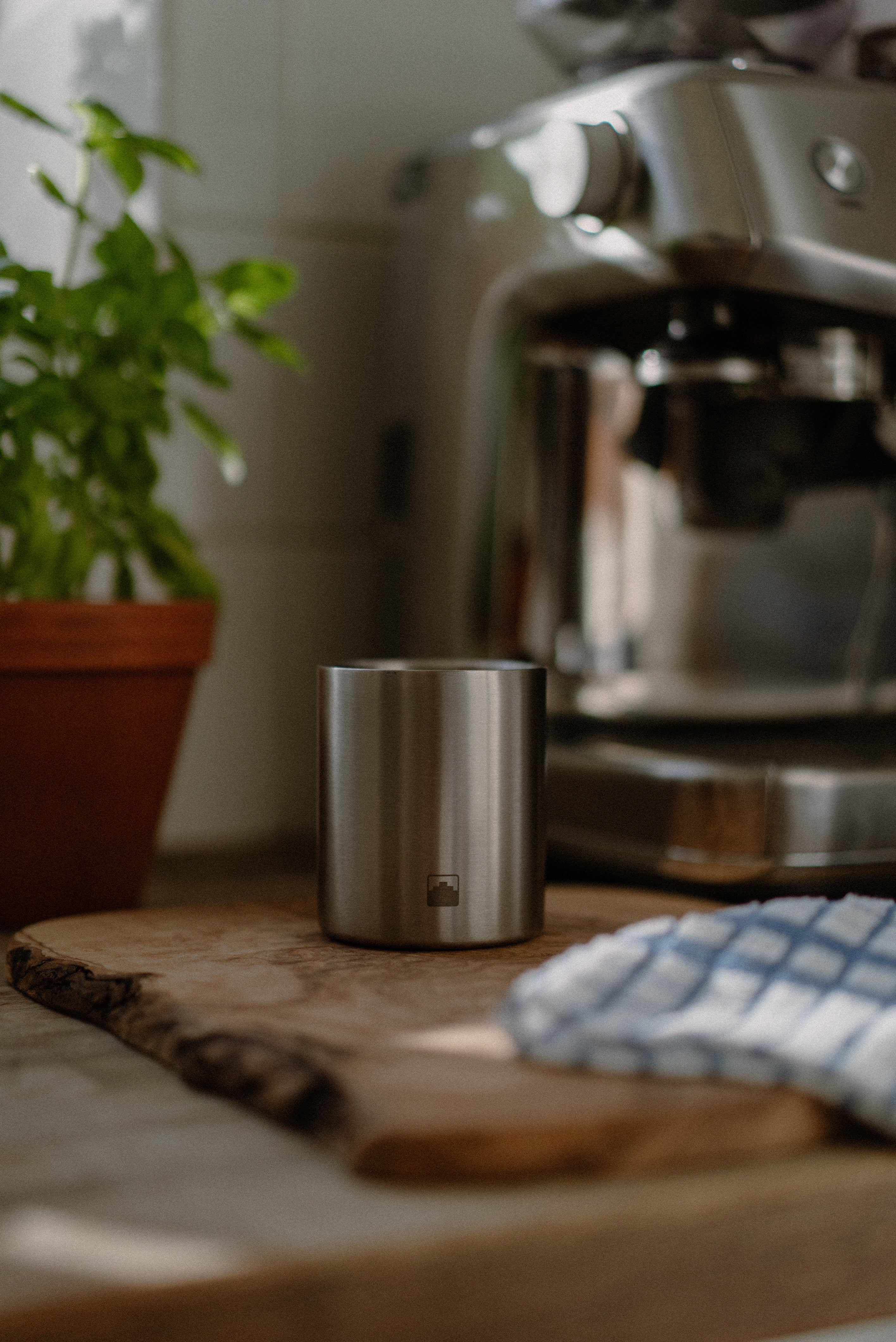 Stainless steel Babel candle on a wooden surface with an espresso machine in the background