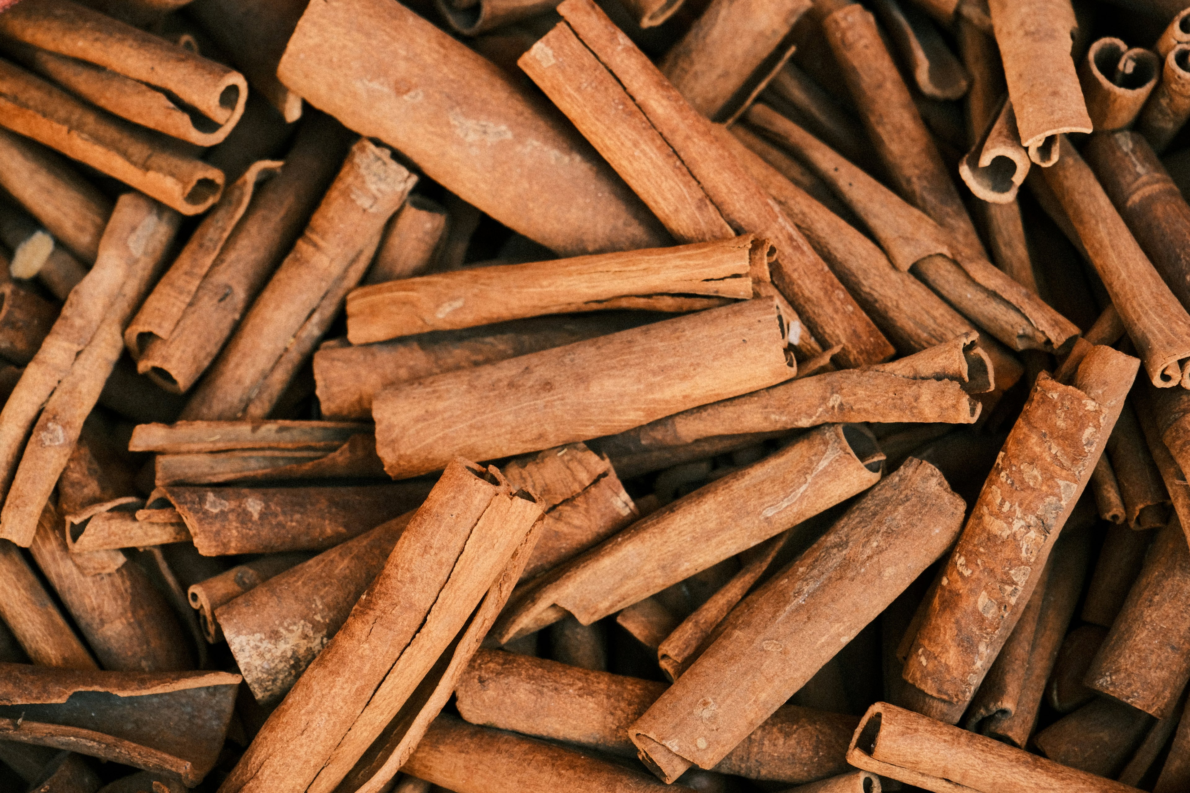 A close-up pile of whole cinnamon sticks with warm brown tones and textured bark.