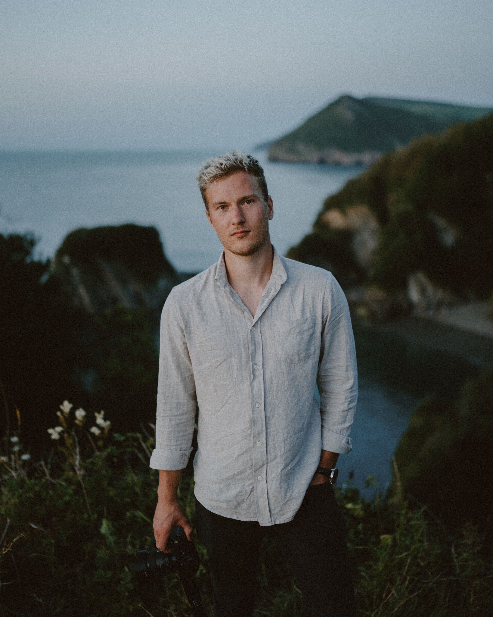 Man standing in a scenic outdoor setting with sea and coastline in the background