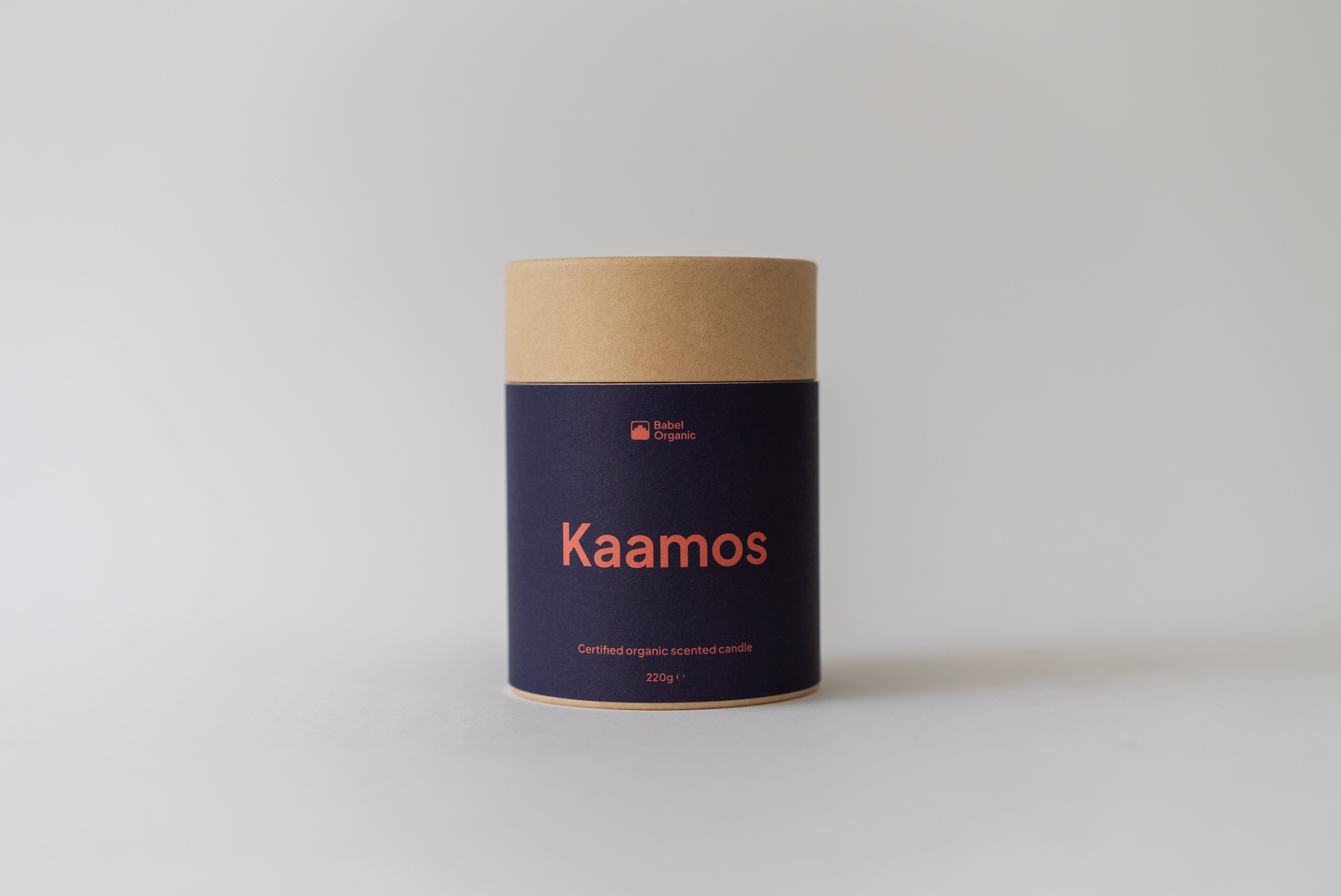 A cylindrical cardboard container with a dark navy blue label and orange text reading 'Kaamos' and 'Bark Candles', photographed on a light gray background.