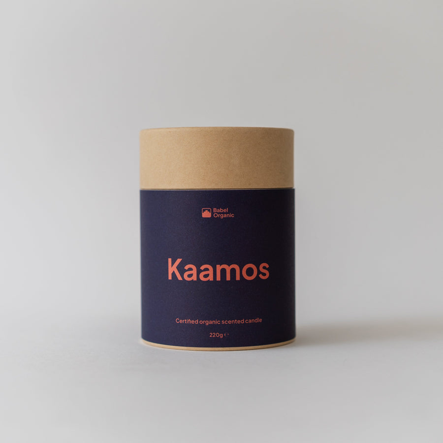 A cylindrical cardboard container with a dark navy blue label and orange text reading 'Kaamos' and 'Bark Candles', photographed on a light gray background.