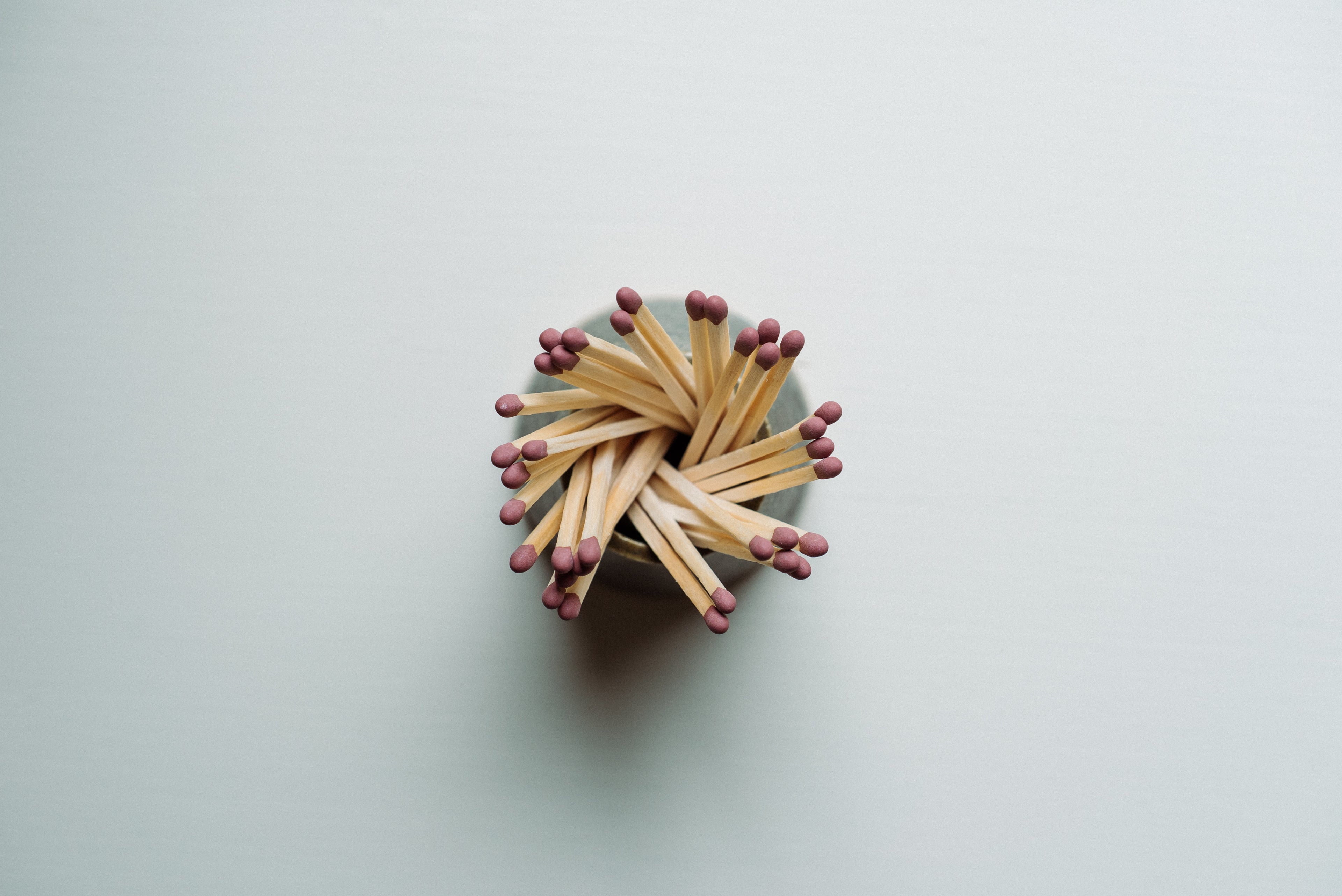 A small bundle of wooden matchsticks with red tips arranged in a circular starburst pattern on a plain light gray background.