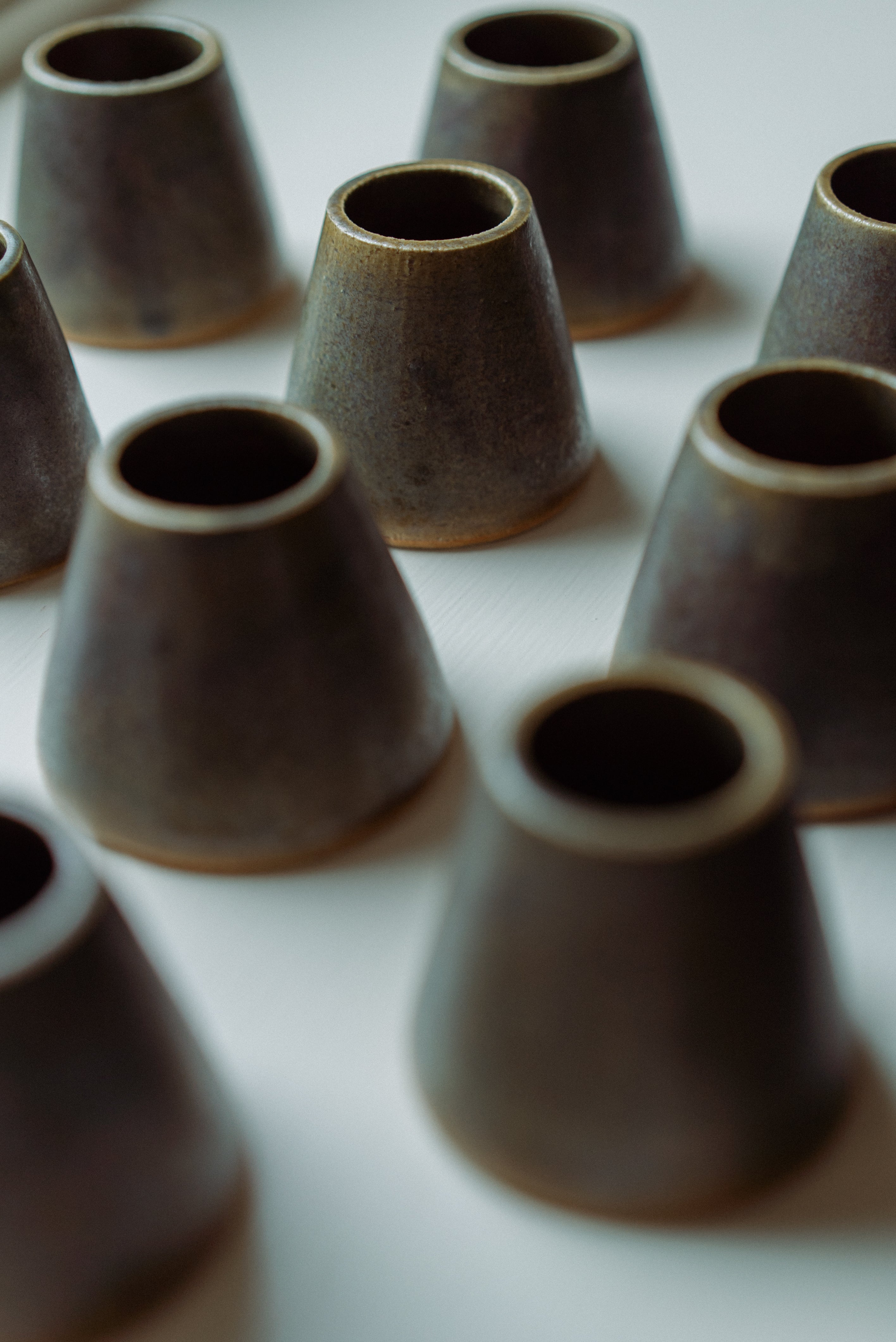 A close-up, shallow depth-of-field view of multiple small, dark brown ceramic match pots arranged on a white surface.